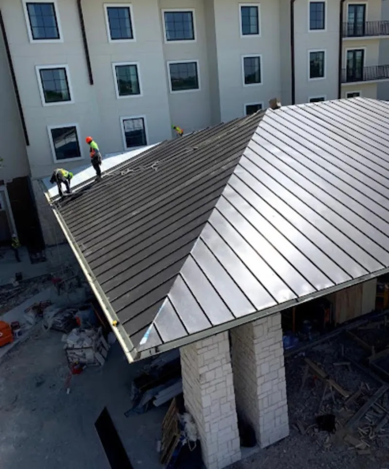 Crew installing standing seam metal roof panels on a commercial project in Webster